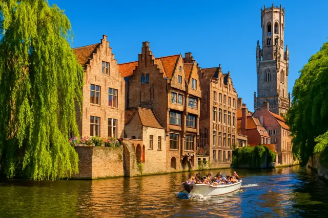 Brugge kanalı, basamaklı cepheli evler ve yeşil ağaçlar